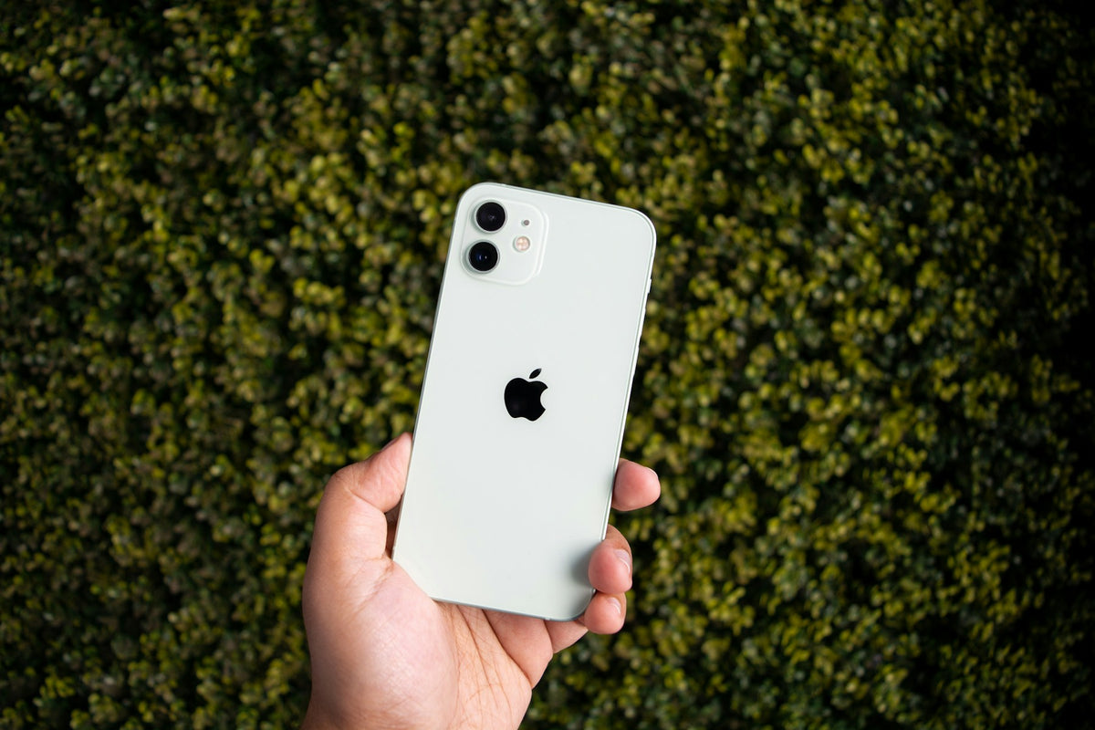 Echte foto van een witte iPhone 12 in de hand, tegen een groene achtergrond